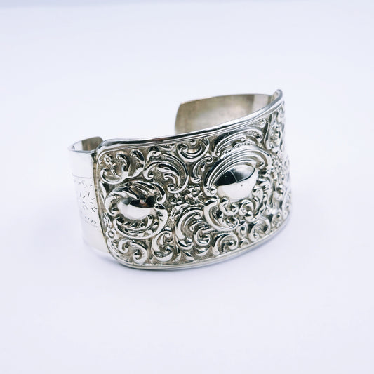 Close-up image of an antique sterling silver cuff bangle featuring ornate engraved detailing, 4cm wide, oval-shaped (70mm x 53mm), weighing approximately 44.5g.