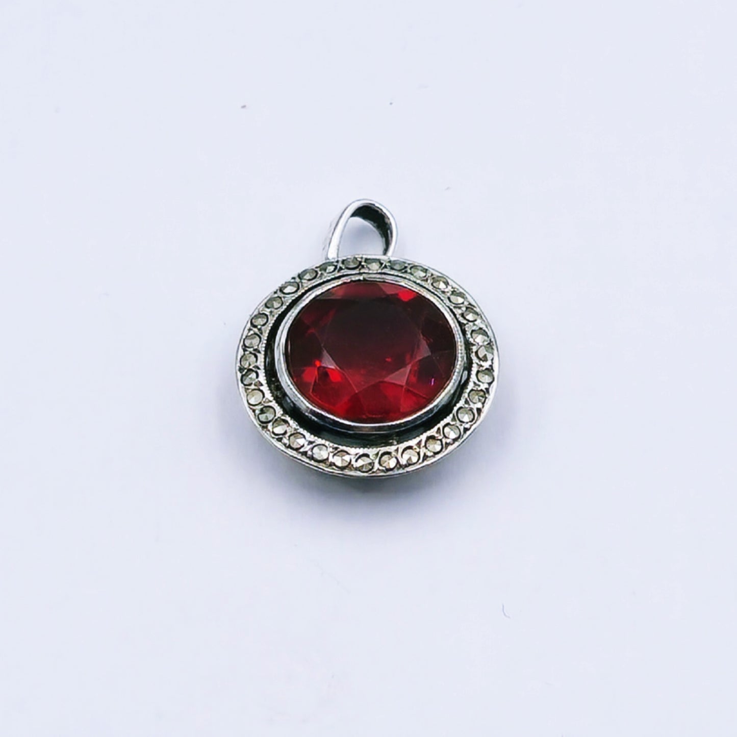 Vintage sterling silver pendant featuring a round red glass stone with a marcasite halo, millgrain edging, and hand-pierced design; approx. 2cm in diameter and 2.9g in weight