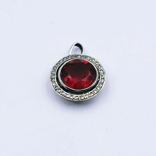 Vintage sterling silver pendant featuring a round red glass stone with a marcasite halo, millgrain edging, and hand-pierced design; approx. 2cm in diameter and 2.9g in weight