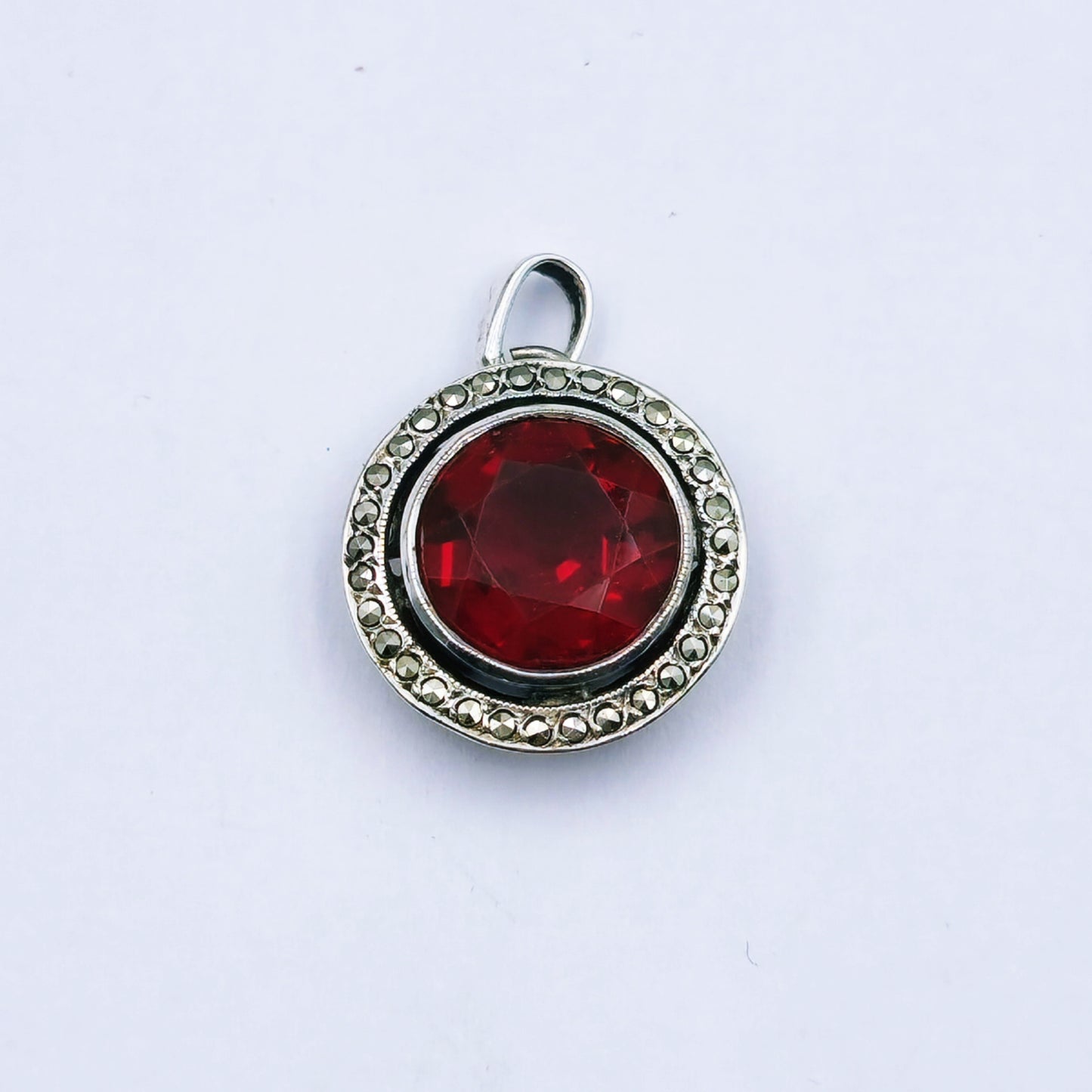 Vintage sterling silver pendant featuring a round red glass stone with a marcasite halo, millgrain edging, and hand-pierced design; approx. 2cm in diameter and 2.9g in weight