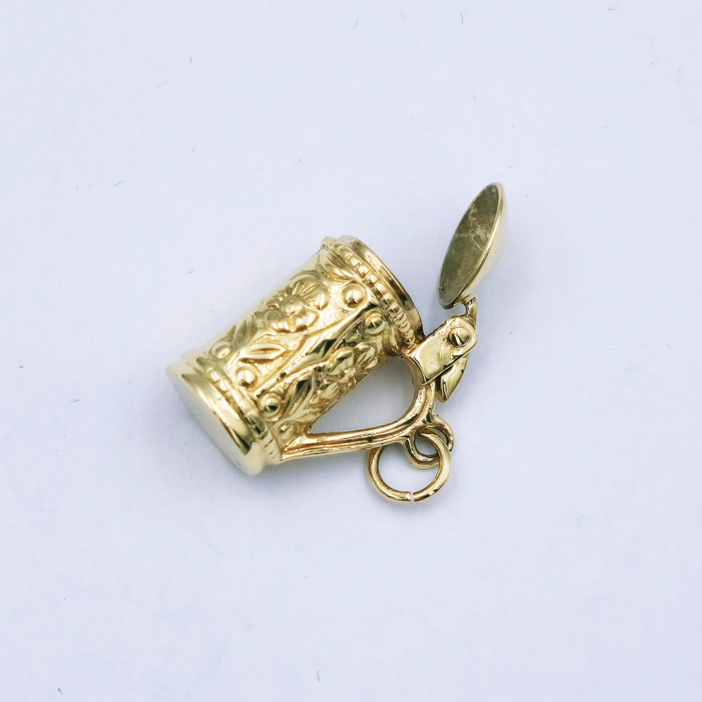 9ct yellow gold beer mug charm with floral design and hinged lid that opens; approx. 16.5mm high by 8mm wide, weighing 3.7g.