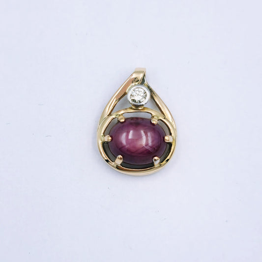9ct yellow gold pendant with a 10mm x 8.5mm oval star ruby in a six-claw setting, accented by a 0.10ct diamond in a white gold tube setting; approx. 3.24g.