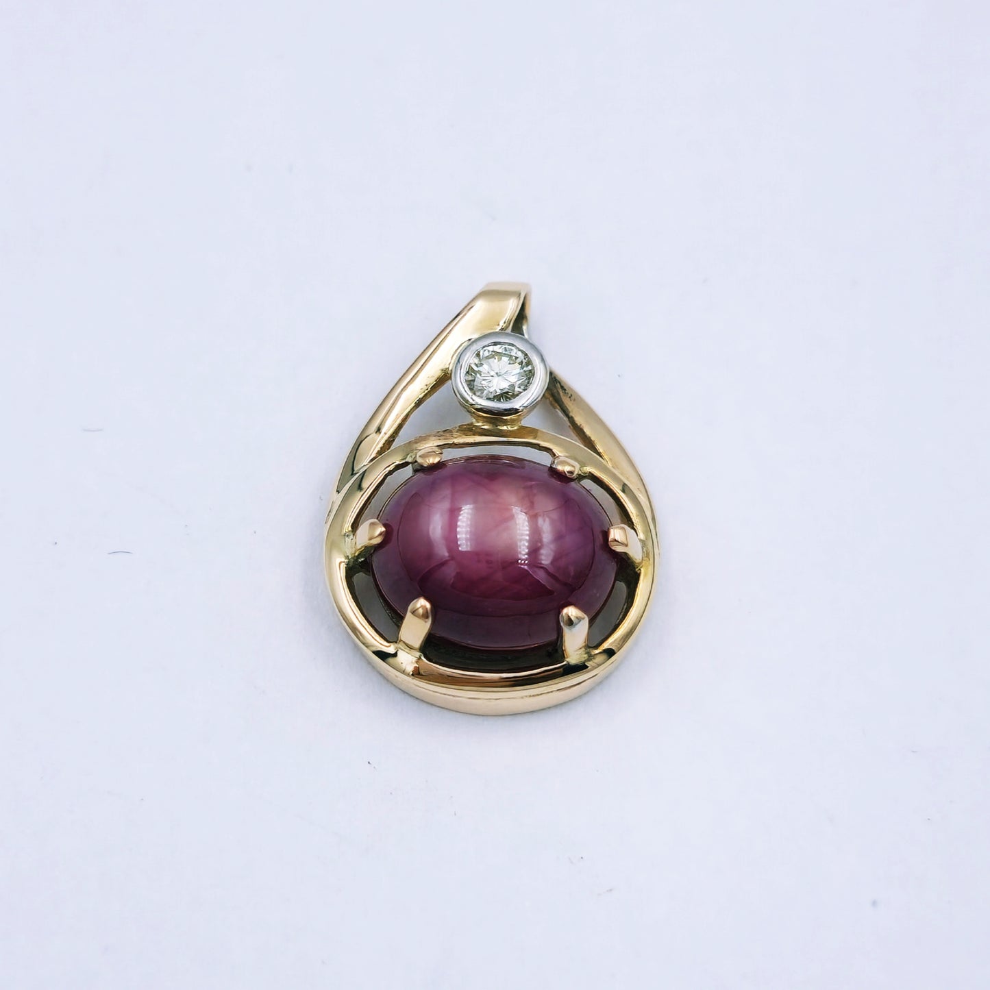 9ct yellow gold pendant with a 10mm x 8.5mm oval star ruby in a six-claw setting, accented by a 0.10ct diamond in a white gold tube setting; approx. 3.24g.