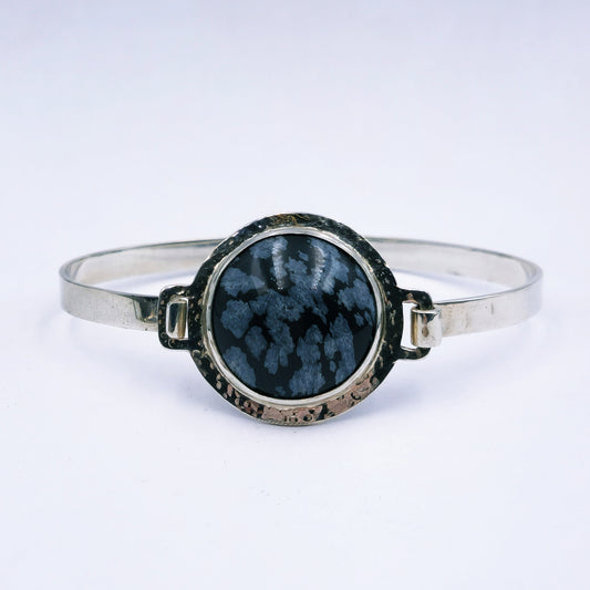 Sterling silver oval bangle with clasp, featuring a 25mm snowflake obsidian set in a hammered round tube bezel, handmade with 74mm diameter.