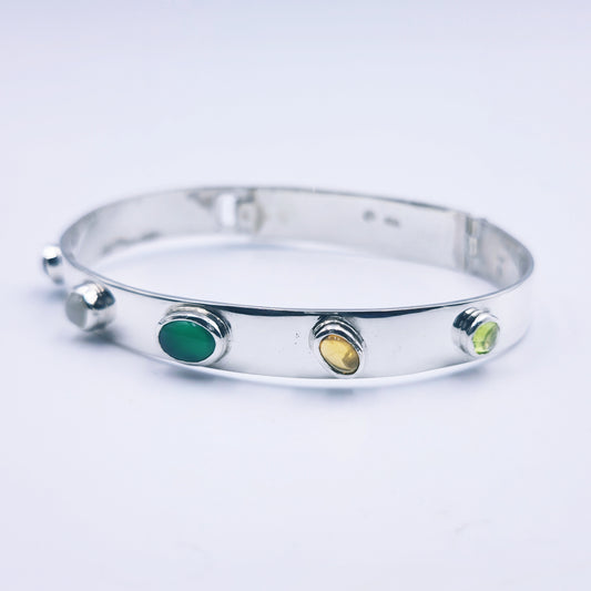 Sterling silver bangle with sky blue topaz, citrine, amethyst, peridot, and garnet in assorted cuts on a half-round band.