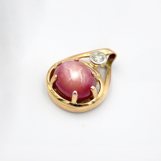 9ct yellow gold pendant with a 10mm x 8.5mm oval star ruby in a six-claw setting, accented by a 0.10ct diamond in a white gold tube setting; approx. 3.24g.