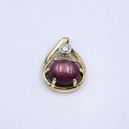 9ct yellow gold pendant with a 10mm x 8.5mm oval star ruby in a six-claw setting, accented by a 0.10ct diamond in a white gold tube setting; approx. 3.24g.
