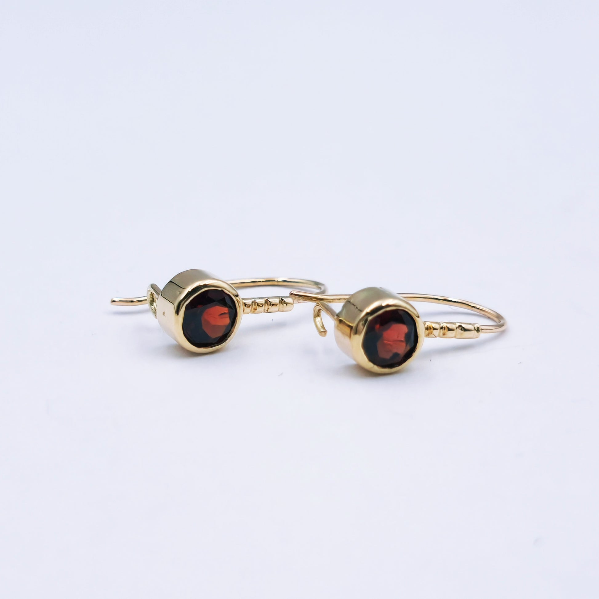 Pair of 9ct yellow gold drop earrings featuring round 5mm garnets in tube settings with beaded shafts and closed shepherd hooks; approx. 1.64g total weight.