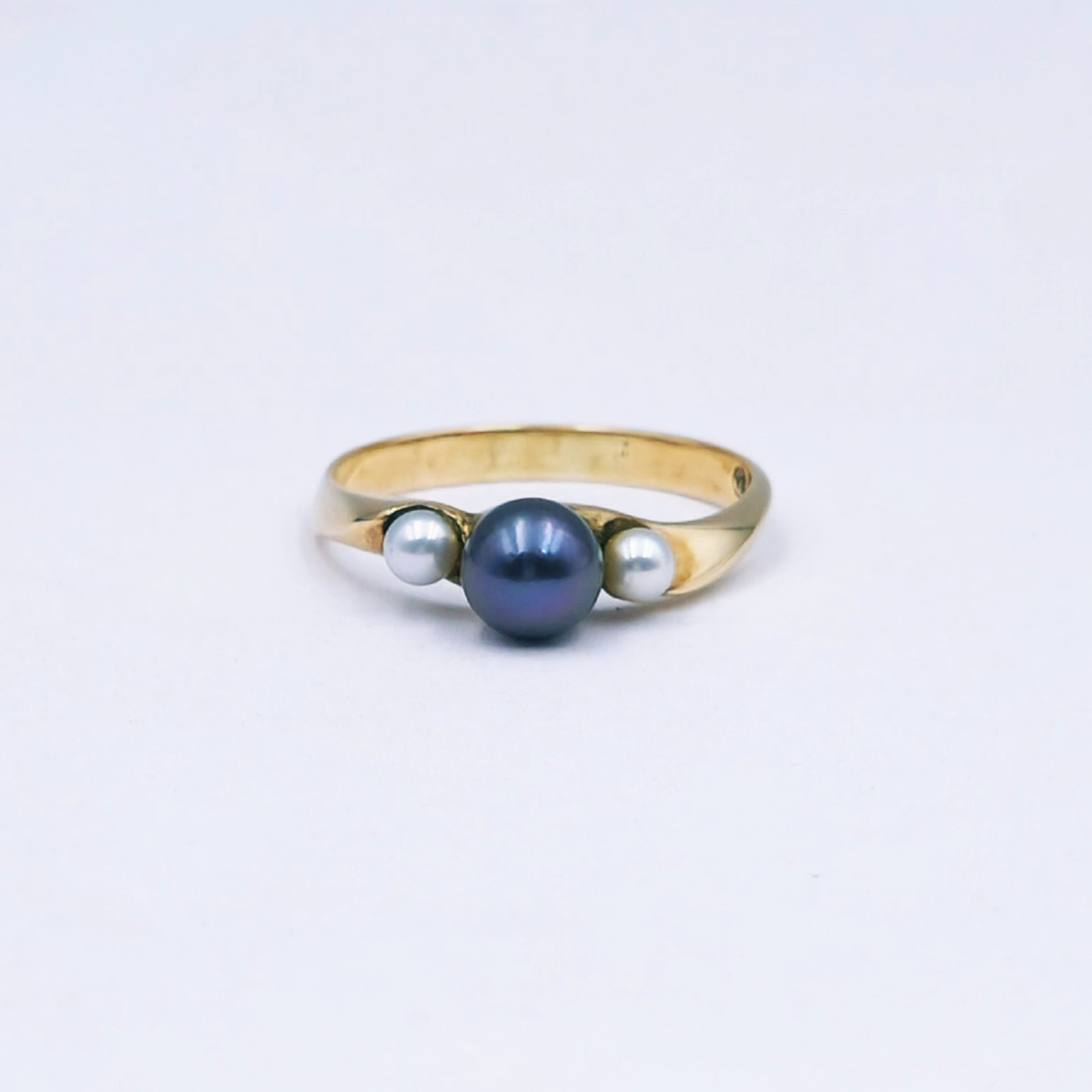 Gold ring with three pearls on a light gray background