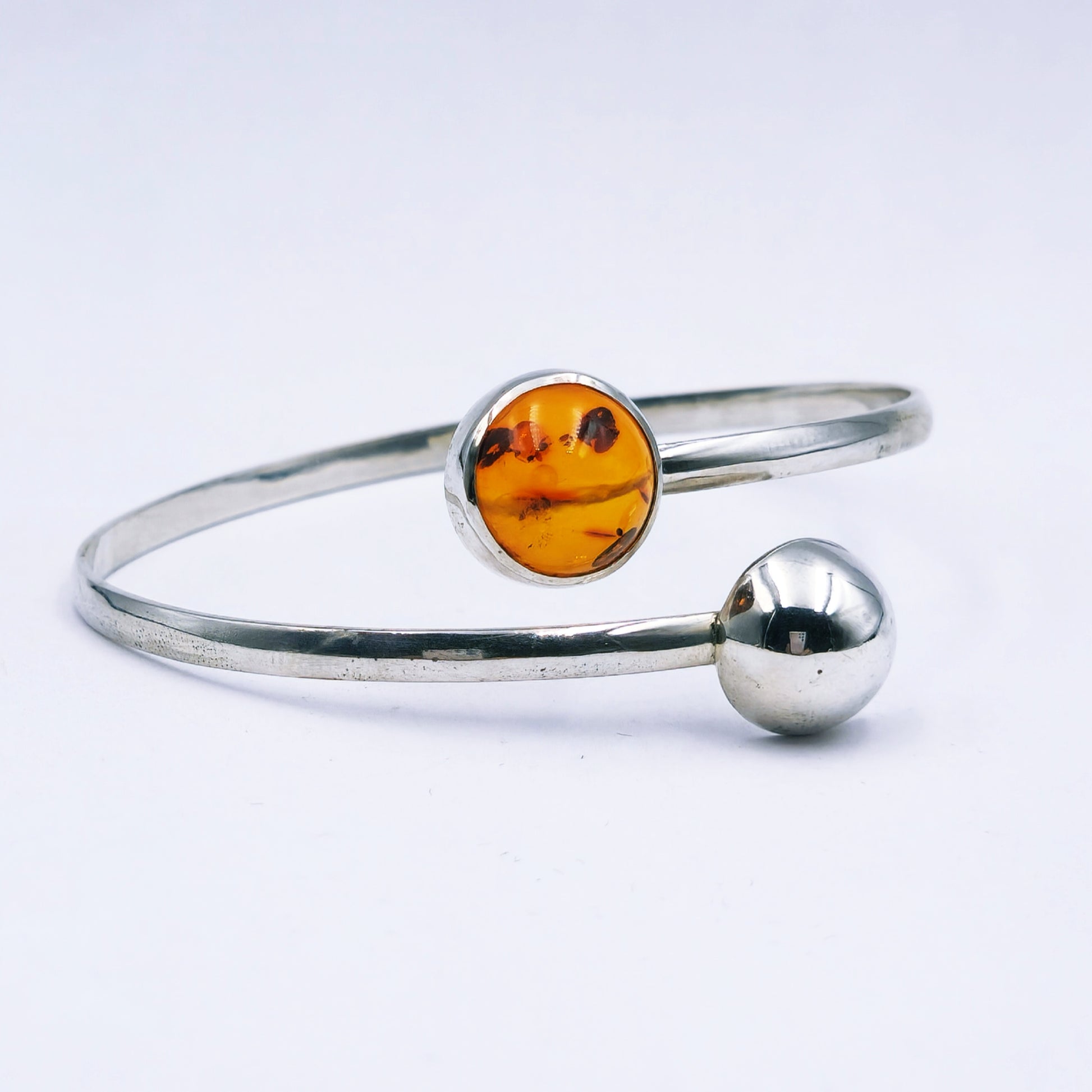 Handmade sterling silver split bangle with amber cabochon in tube setting and silver half dome detail,