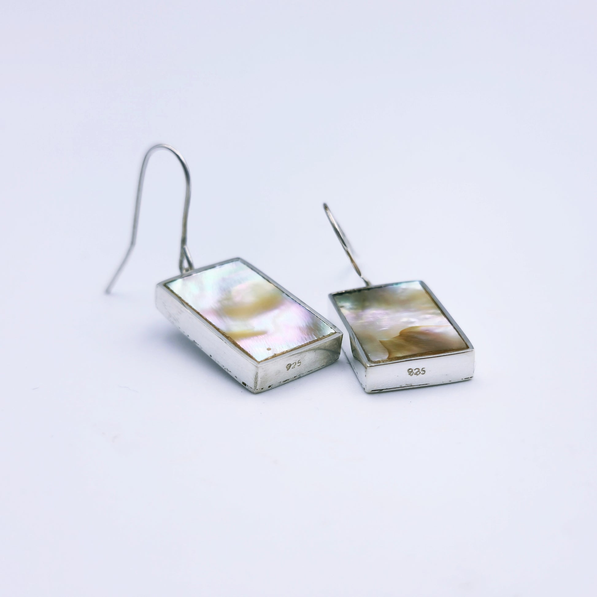 Sterling silver abalone earrings with blue and pink/grey peacock tones, set in rectangular frames and hanging from shepherd hooks.
